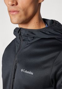 Giacca Columbia nera con chiusura zip, colletto alto e superficie liscia. Logo in bianco sul petto.