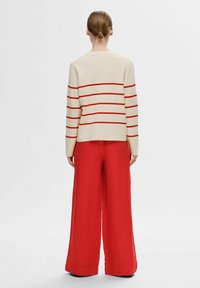 Beige Pullover mit roten horizontalen Streifen, kombiniert mit weit geschnittenen roten Hosen, die ein entspanntes und modernes Design verkörpern.