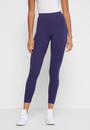 Fioletowe legginsy wykonane z elastycznego materiału, w wysokiej talii i gładkiej teksturze, w połączeniu z białymi butami sportowymi.