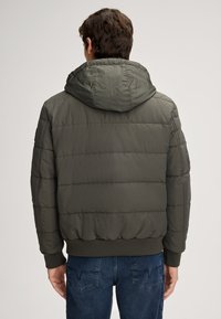 Giubbotto imbottito verde oliva con cappuccio, caratterizzato da cuciture trapuntate, polsini a coste e vita a coste, abbinato a jeans in denim blu.