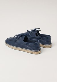 Zapatos de barco de cuero azul marino con diseño de cordones, suela de cuerda de yute y ojales en tono plateado. Textura suave con forma de punta redondeada.