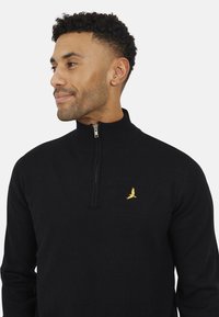 Maglione zip-up nero con collo alto. Presenta un piccolo emblema di un uccellino giallo sul petto. Realizzato in un morbido tessuto testurizzato.