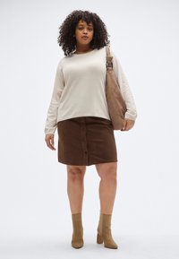 Hellbeiges Langarmshirt, brauner Cord-Rock mit Knöpfen, braune Stiefeletten mit Absatz und eine passende Umhängetasche. Glatte Textur und lässige Passform.