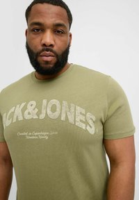 Olivegrünes Baumwoll-T-Shirt mit großem, hellen "BACK&JONES"-Text und kleinerem Text darunter. Mit kurzen Ärmeln und Rundhalsausschnitt.