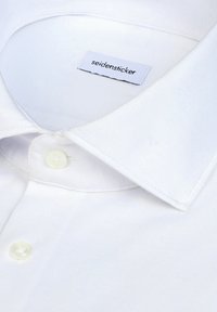 Chemise blanche à boutons avec un col pointu et des boutons blancs visibles, avec une étiquette de marque "seidensticker" à l'intérieur du col.