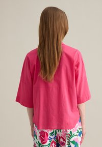 Blusa a maniche corte, leggera, di un vivace colore rosa fucsia, con una vestibilità ampia e orlo dritto, abbinata a pantaloni a fantasia floreale colorati.