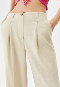 Beige linbyxor med en avslappnad passform, med framfickor, knappstängning och sidofickor. Slät textur med diskret lyster.
