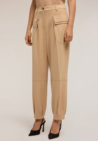 Pantalons beiges sur mesure avec poches latérales, pr�ésentant une coupe décontractée, une texture lisse et des ourlets retroussés, associés à des escarpins noirs à bout pointu.