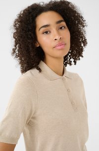 Beige polo shirt van zacht materiaal, met een kraag en drie knopen, korte mouwen en een gestructureerd breipatroon.
