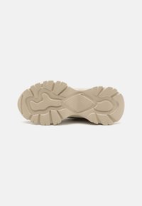 Semelle de sneaker beige clair avec une surface texturée, présentant un motif de semelle proéminent pour l'adhérence et un détail central en forme de diamant.