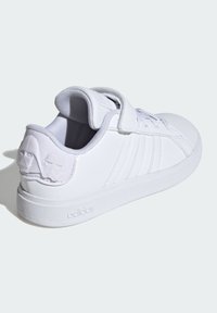 Baskets blanches avec une tige synthétique lisse, trois rayures sur le côté, une sangle velcro, un col rembourré et un accent en forme de personnage moulé au niveau du talon.