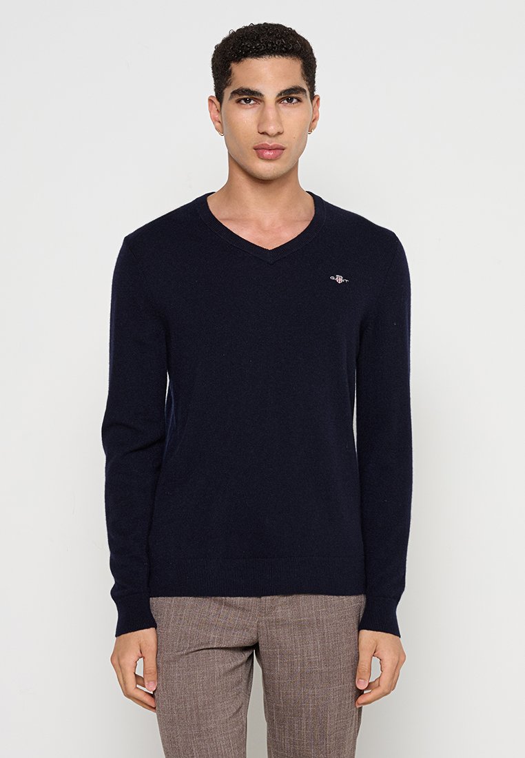 Navyblauer V-Ausschnitt-Pullover aus weichem Stoff; mit kleinem Logo auf der Brust; taillierte Passform mit langen Ärmeln und gerippten Bündchen.