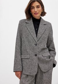 Sivý károvaný blazer s priliehavým strihom, klopovými goliermi, dvoma gombíkmi a záklopkovými vreckami. Textúrovaná látka so štruktúrovanou siluetou.