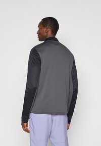 Szara i czarna kurtka na zamek błyskawiczny z długimi rękawami, kołnierzykiem oraz teksturowanym materiałem na plecach. Posiada gładki czarny akcent na rękawach.