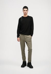 Sweater preto de malha texturizada, calças khaki de corte slim e sapatilhas pretas. Design minimalista com um ajuste descontraído e detalhes subtis.