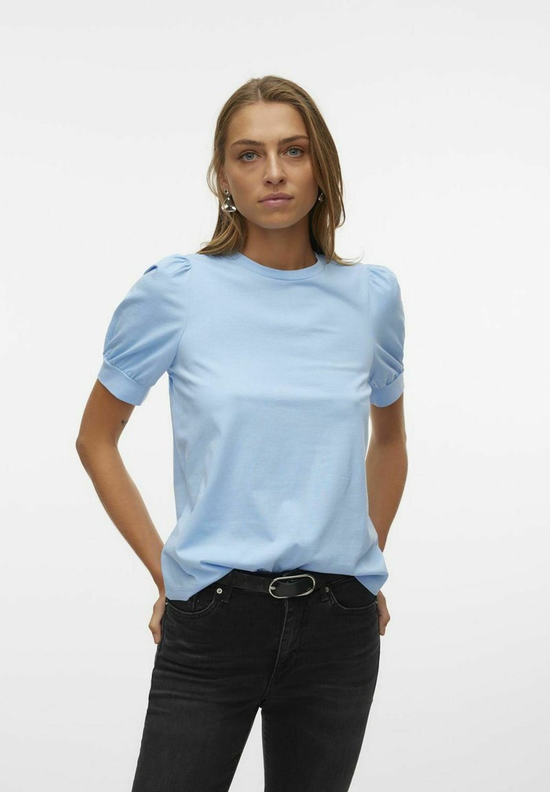 T-shirt azul claro de manga curta com mangas bufantes, decote redondo, feito de um tecido macio, combinado com jeans pretos justos e um cinto.