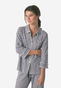 Navy og hvidt ternet pyjamas i gingham-mønster, med en flæsekrave, knapfront og hjertebroderi på brystet. Løs pasform.
