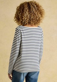 Prúžkované dlhé rukávy tričko v krémovej a námorníckej farbe, s výstrihom do lodi a voľným strihom, v kombinácii s modrými džínami.