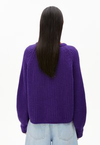 Lila gerippter Strickpullover mit lockerer Passform und langen Ärmeln. Verfügt über einen runden Halsausschnitt und strukturierter Stoff. Getragen mit hellen Denimshorts.