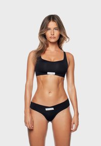 Set di bikini nero con bralette a spalline larghe e un'etichetta che recita "GOD SAVE QUEENS", abbinato a un slip a vita bassa.