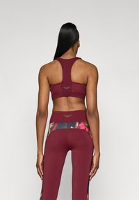 Sārtinā brūns sporta krūšturis un legingi. Krūšturis ar sacīkšu aizmuguri; legingi ar ziedu apstādījumiem. Gluda, elastīga auduma.