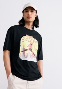 T-shirt noir en coton avec un graphique coloré d'un joueur de basket et le texte "AIR JORDAN", à manches courtes et à coupe décontractée.