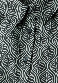 Tessuto a motivi foglia neri e bianchi caratterizzato da un design con colletto e due bottoni, che mette in risalto una texture morbida e dettagli intricati.