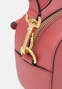 Borsa in pelle rossa con zip dorata, hardware prominente e bordi neri a contrasto. Superficie testurizzata con una finitura liscia.