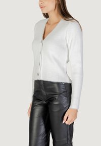 Cardigan bianco, morbido e a coste con scollatura a V profonda e cinque bottoni decorativi. Dotato di maniche lunghe e vestibilità leggermente cropped.