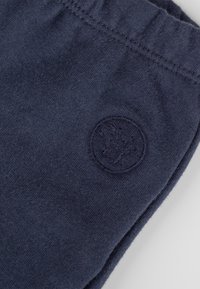 Tessuto blu scuro con un emblema circolare ricamato che presenta un design di foglia d'acero vicino a una cucitura.