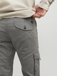 Gray cargo pants featuring reinforced stitching, a buttoned back pocket, and a side pocket with flap. Fabric appears smooth and durable.
