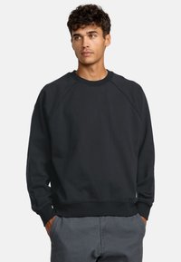Czarny sweter crewneck z raglanowymi rękawami i ściągaczami. Wykonany z miękkiego materiału, o luźnym kroju. Uzupełniające szare spodnie.