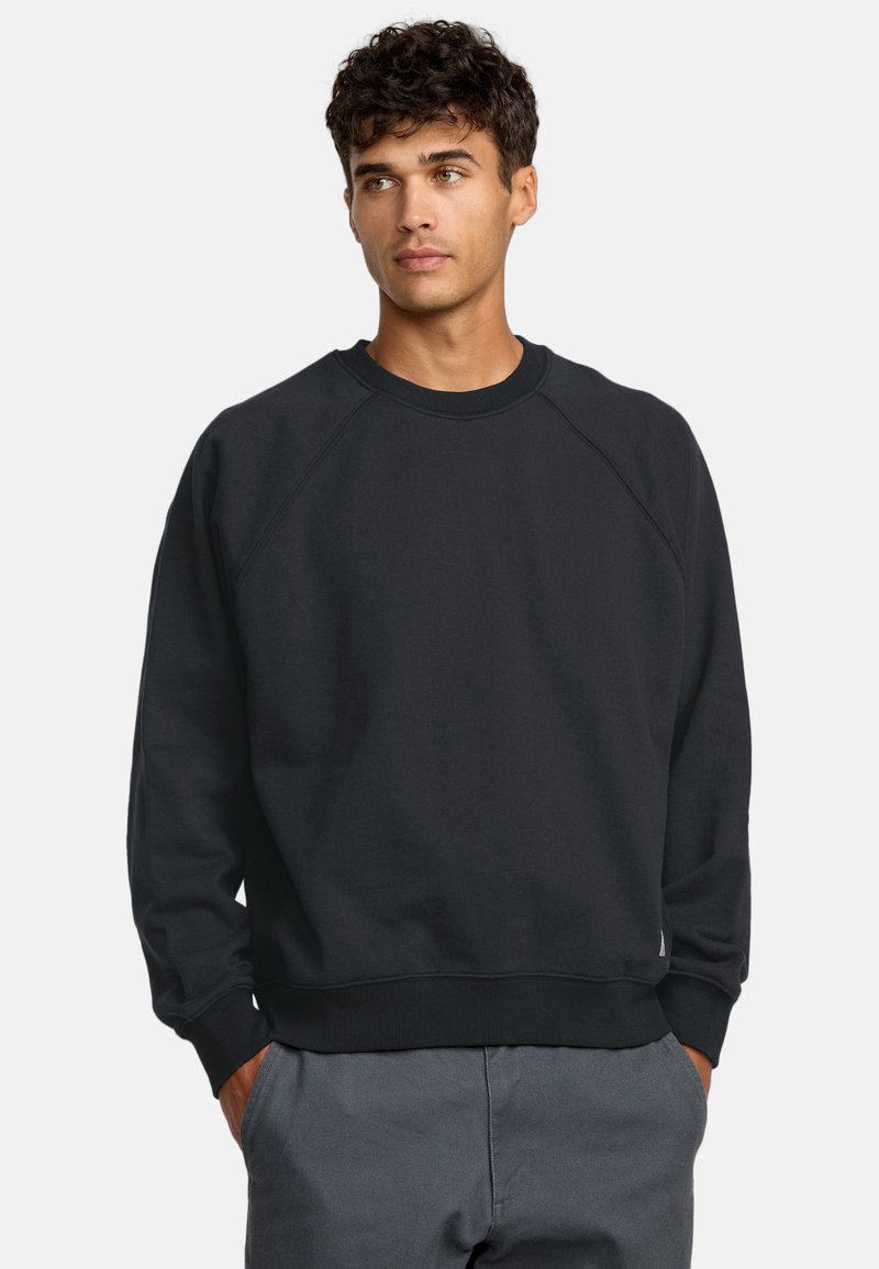 Czarny sweter crewneck z raglanowymi rękawami i ściągaczami. Wykonany z miękkiego materiału, o luźnym kroju. Uzupełniające szare spodnie.