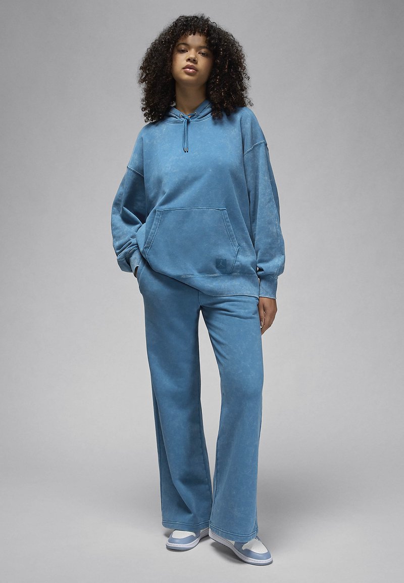 Hoodie en coton bleu avec une poche avant et un cordon de serrage, associé à un pantalon large assorti. Texture lisse avec un aspect délavé.
