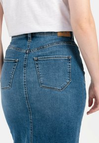 Mørkeblå denimnederdel med en tætsiddende pasform, høj talje, synlige sømme, to baglommer og et læderlabel på taljebåndet.