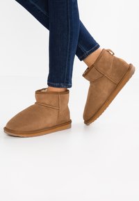 Stivaletti in suede marrone con punta rotonda, dettagli cuciti e suola in gomma, abbinati a jeans fitted blu scuro.