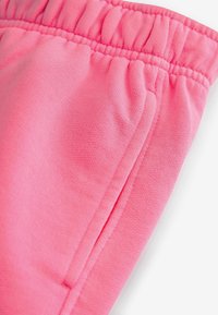 Närbild av rosa elastisk midjebandstyg med en sidofickseam på mjuka texturerade byxor.