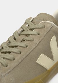 Κοντινό πλάνο σε μπεζ σουέντ αθλητικό παπούτσι με κορδόνια ίδιου χρώματος και κρεμ λογότυπο "V" στο πλάι, με ραμμένες λεπτομέρειες και σόλα από καουτσούκ.