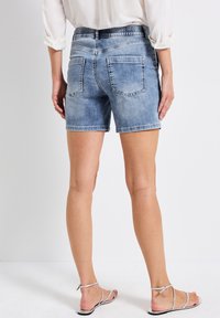 Hellblaue Denim-Shorts mit elastischem Bund, ausgestattet mit zwei Gesäßtaschen und geradem Schnitt, kombiniert mit silbernen Riemchensandalen.