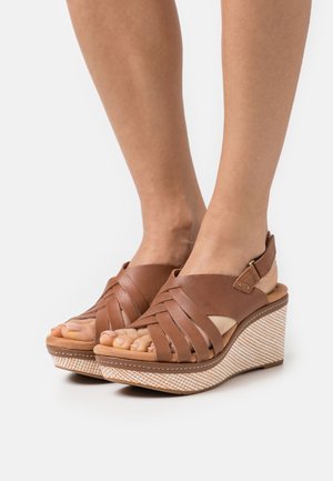 Brown leather wedge sandals feature crisscross straps, an open toe, and a textured platform with a woven pattern for added detail.