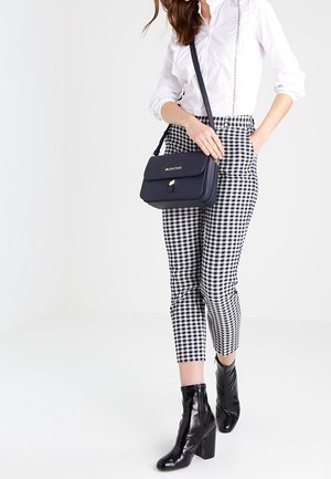 Pantaloni a scacchi bianchi e neri, dalla forma aderente, abbinati a una camicia bianca con bottoni e stivali neri alla caviglia. Una piccola borsa blu navy completa il look.