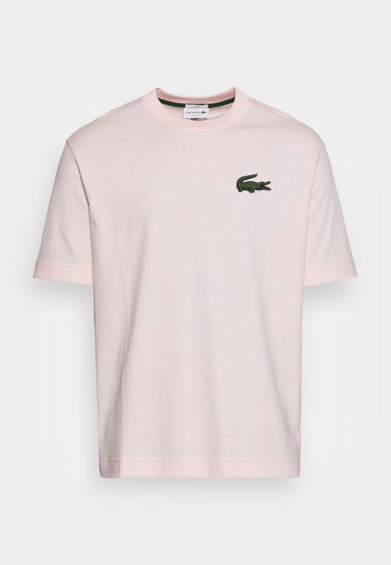 T-shirt en coton rose clair avec un col rond, des manches courtes et un logo de crocodile brodé vert sur la poitrine gauche.