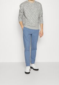 Šedá mikina s vyvýšeným geometrickým vzorem, spárovaná se světle modrými, přiléhavými kalhotami a bílými botami s černými podrážkami.