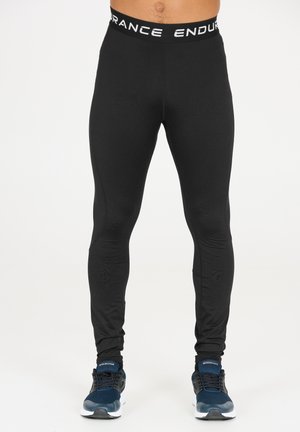 Zwarte sportleggingen met een aansluitend ontwerp en een elastische tailleband met daarop de witte tekst "ENDURANCE". Draagt met marineblauwe sneakers.