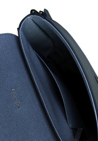 Interiér tašky z texturované tmavě modré látky obsahuje více přihrádek a hladký lem. Vyduté logo se nachází na dně.
