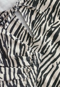 Gros plan d’un tissu imprimé zèbre noir et blanc avec des coutures froncées et un détail de nœud noué sur un matériau doux.