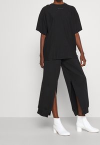 Svart oversized t-shirt och vida byxor med sidöppningar, tillverkade av mjukt tyg. Matchas med vita ankelskor med klack.