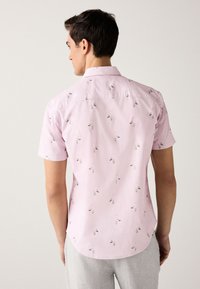Chemise à manches courtes en coton rose clair avec un motif floral. Comprend un col, une patte de boutonnage et un ourlet arrondi.