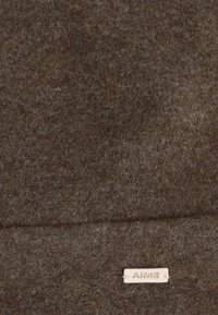 Tessuto in feltro di lana marrone con una superficie morbida e un'etichetta prominente che recita "AIME" in un colore chiaro, posizionata sul bordo inferiore.