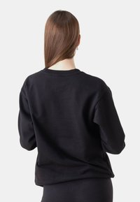 Sudadera negra con un corte relajado, cuello acanalado y mangas largas, con una textura suave y costuras mínimas visibles en la parte posterior.